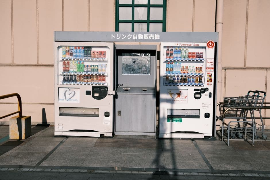 壁際に設置された白いドリンク自動販売機。ジュースや缶コーヒーが並んでいる