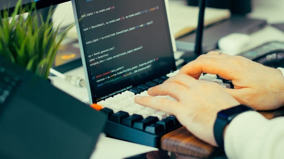 キーボードでコードを入力する手元と、スクリプトが表示された画面