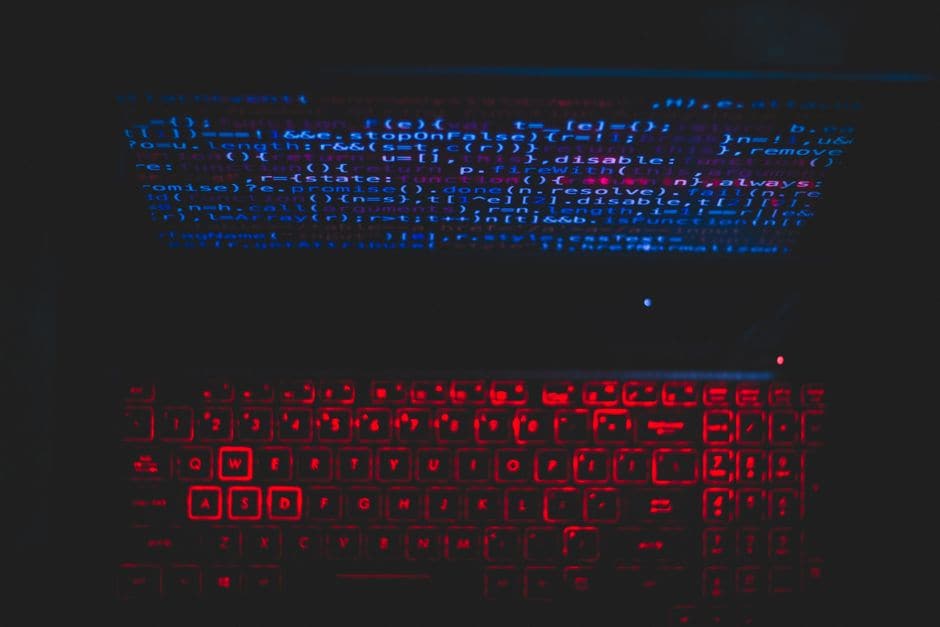 赤いバックライトのキーボードと、コードが表示された画面を暗い室内で撮影した写真