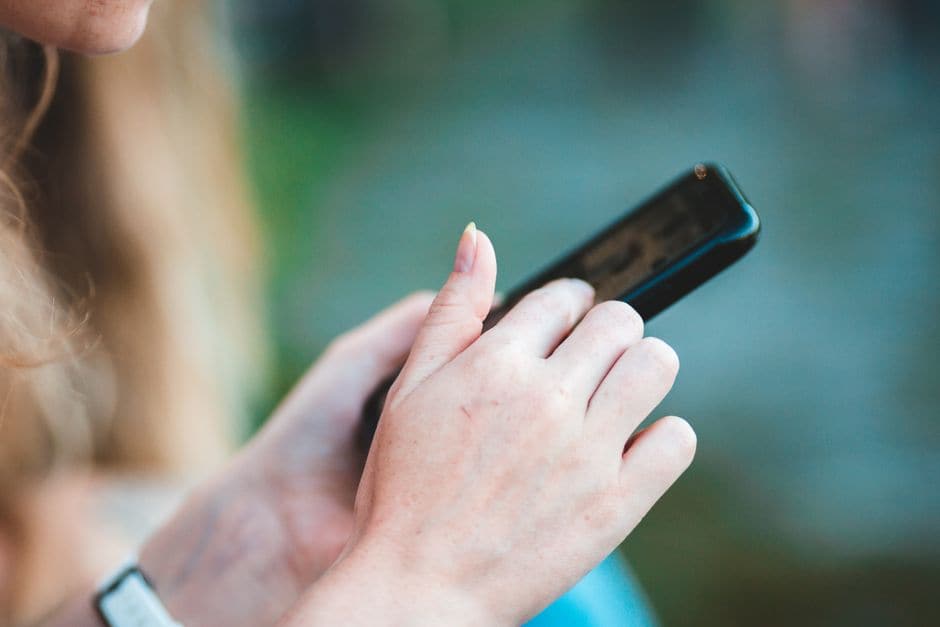 イメージ写真。スマートフォンを両手で持ち、画面に指先で触れている接写。画面の表示内容は判読できない。