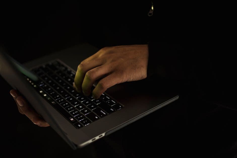 暗い部屋でノートパソコンのキーボードを打つ手元を撮った写真