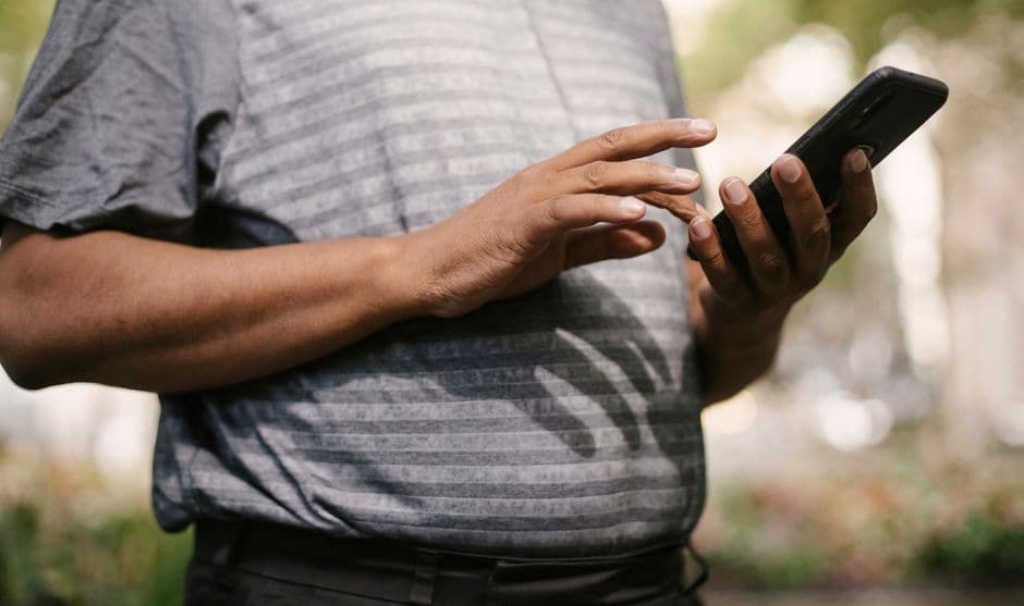 屋外でスマートフォンの画面を指先で操作している人の手元(イメージ写真)