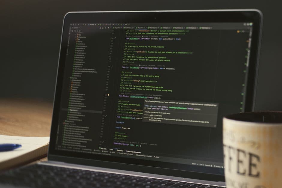 暗い部屋でコーヒーを脇に置き、ノートパソコンでコードを表示している様子