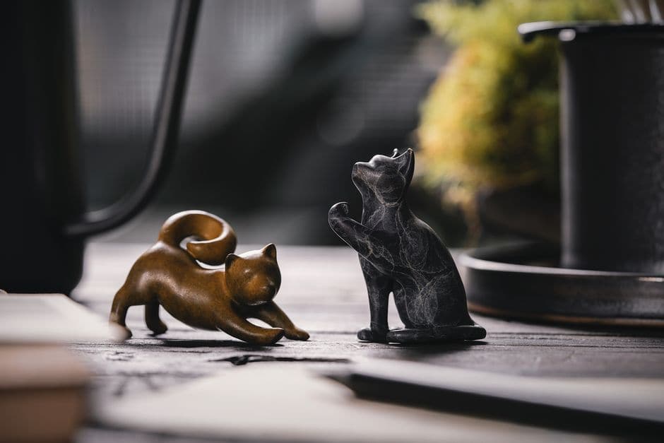 木目のテーブルに置かれた、金色と黒の猫の置物2体