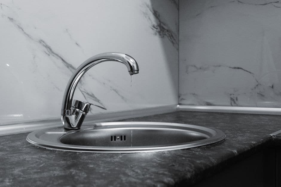 大理石調の壁を背にした、水が滴る銀色のキッチン蛇口と丸いシンクの写真