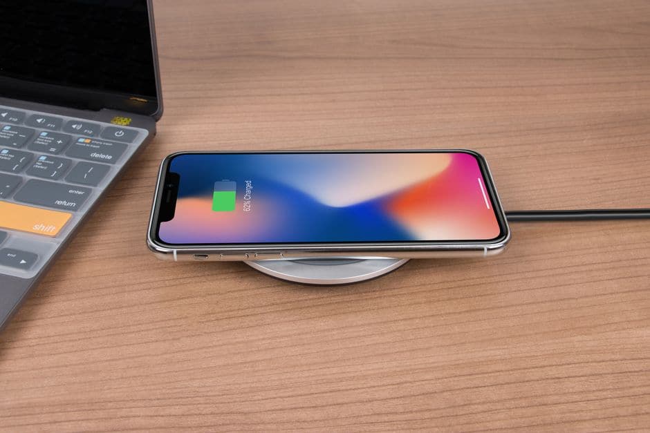 スマートフォンが円形のワイヤレス充電パッドの上に置かれ、ノートパソコンの脇で充電されている様子
