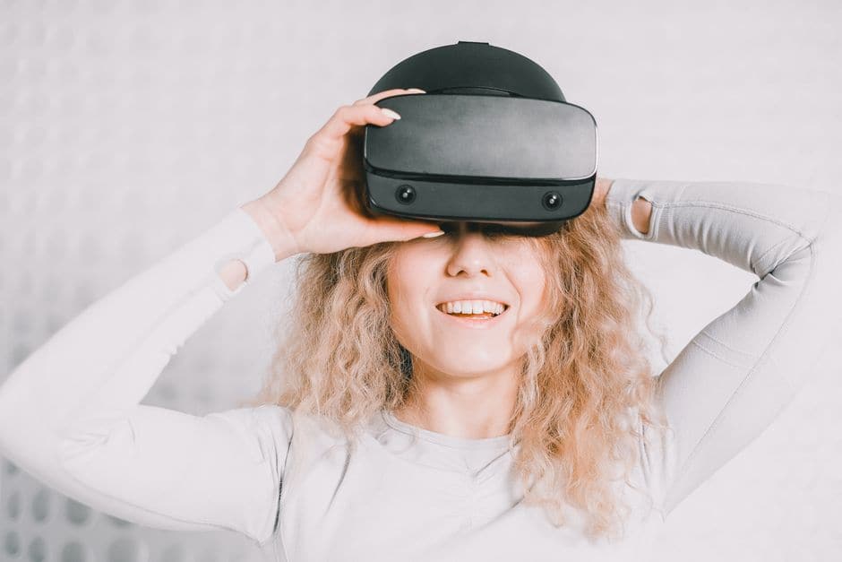 黒いVRヘッドセットを両手で頭にかぶり、笑顔を見せる人物の写真
