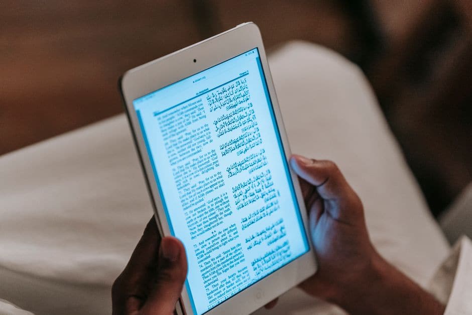 白いタブレットを手に持ち、画面に表示された文章を読んでいる様子
