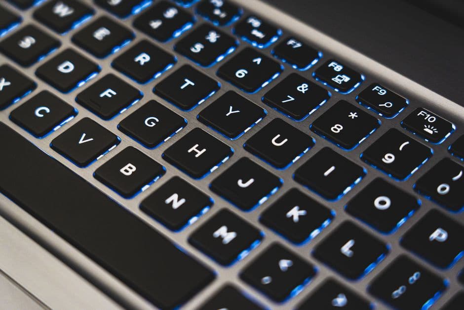 青いバックライトに照らされたノートパソコンのキーボードを斜め上から写した接写