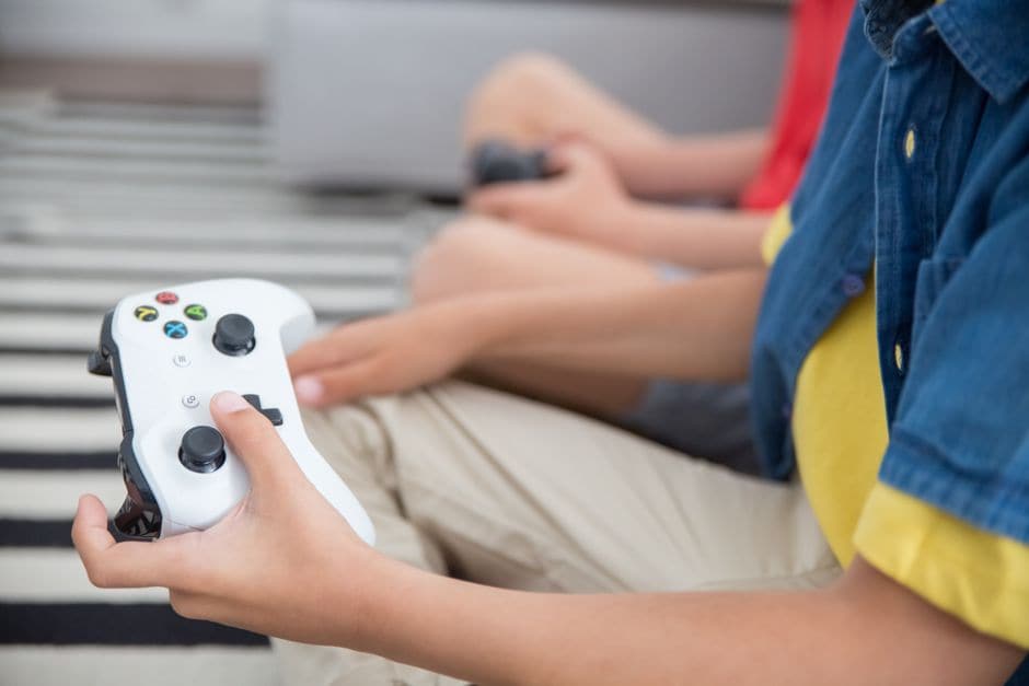 子どもが白いゲームコントローラーを両手で握り、ボタンを操作している接写