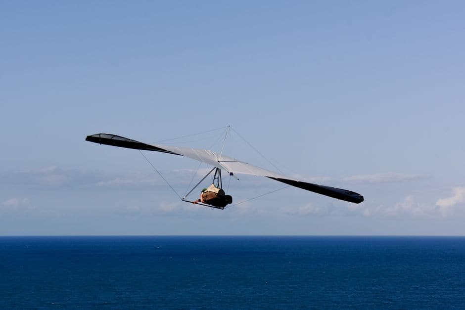 青空と海を背景に、1人乗りのハンググライダーが気流に乗って滑空している