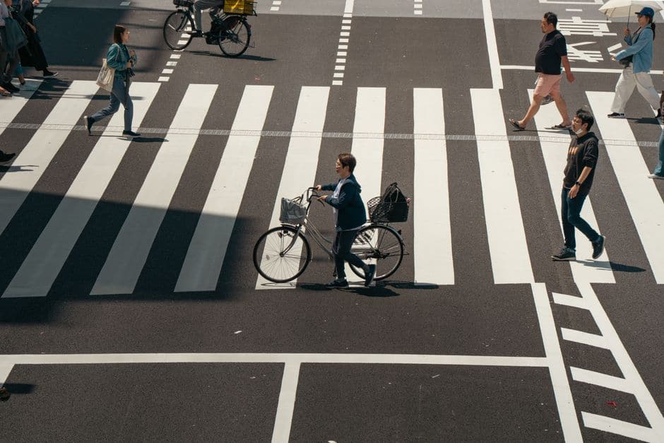 東京の交差点の横断歩道を、自転車を押して渡る人と歩行者たちを上空から撮った写真