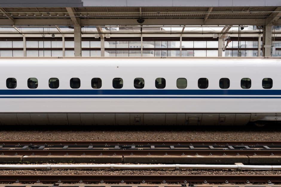 線路脇から見た、青い帯の入った白い新幹線車両の側面の写真
