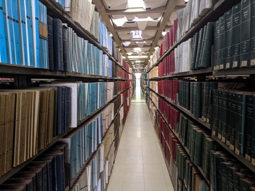 イメージ写真。色分けされた製本雑誌が奥まで並ぶ、見通しのいい図書館の書架の通路。