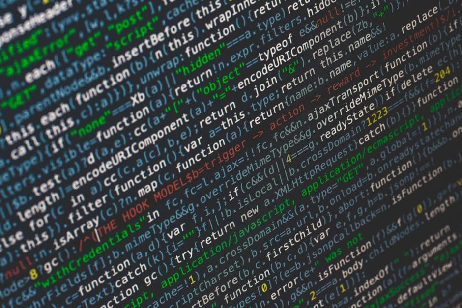 暗い背景のモニターに映る、色分けされたJavaScriptのプログラムコードのクローズアップ(イメージ写真)