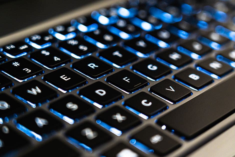 バックライトが光るノートパソコンのキーボードを斜め上から写したクローズアップ